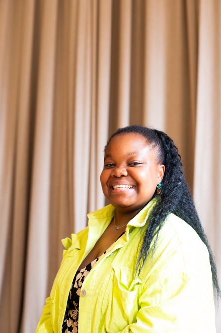 Photo of Corinne Walker, the Artist Development Producer and Facilitator for Beyond face, stood infront of a curtain and looking directly into the camera and smiling
