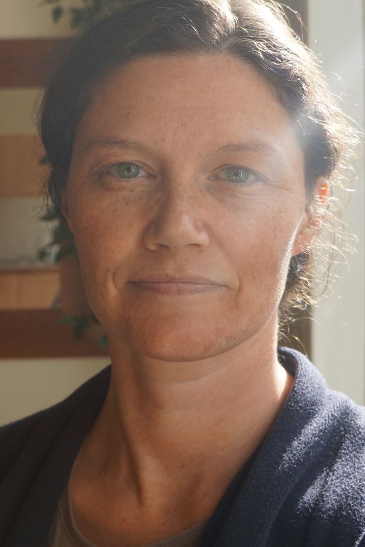 A headshot of a woman with short brown hair and green eyes, she is smiling directly at the camera
