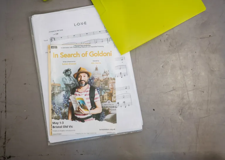 A music sheet is on the floor with flyers for a theatre show called In Search of Goldoni rest on top