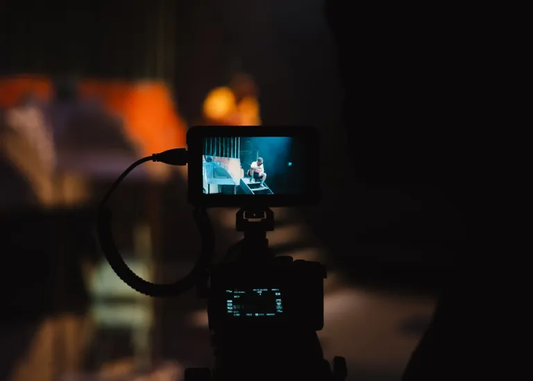 A camera records a performance on a stage in the distance