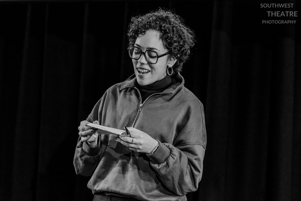 A woman with short curly hair and glasses smiles and reads a speech she is holding in her hands