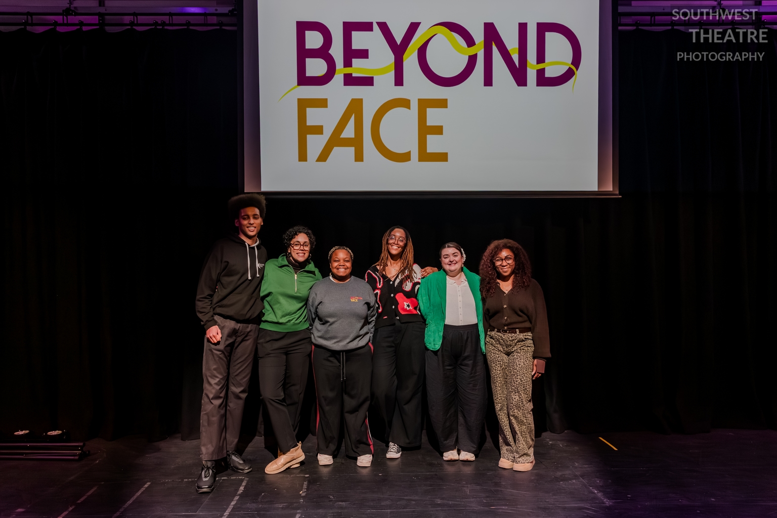 A group of 6 people stand in front of a screen reading Beyond Face, they're stood in a line smiling