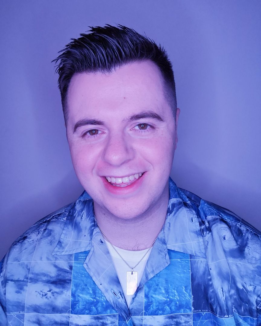 A man with short brown hair and a blue shirt smiles directly at the camera