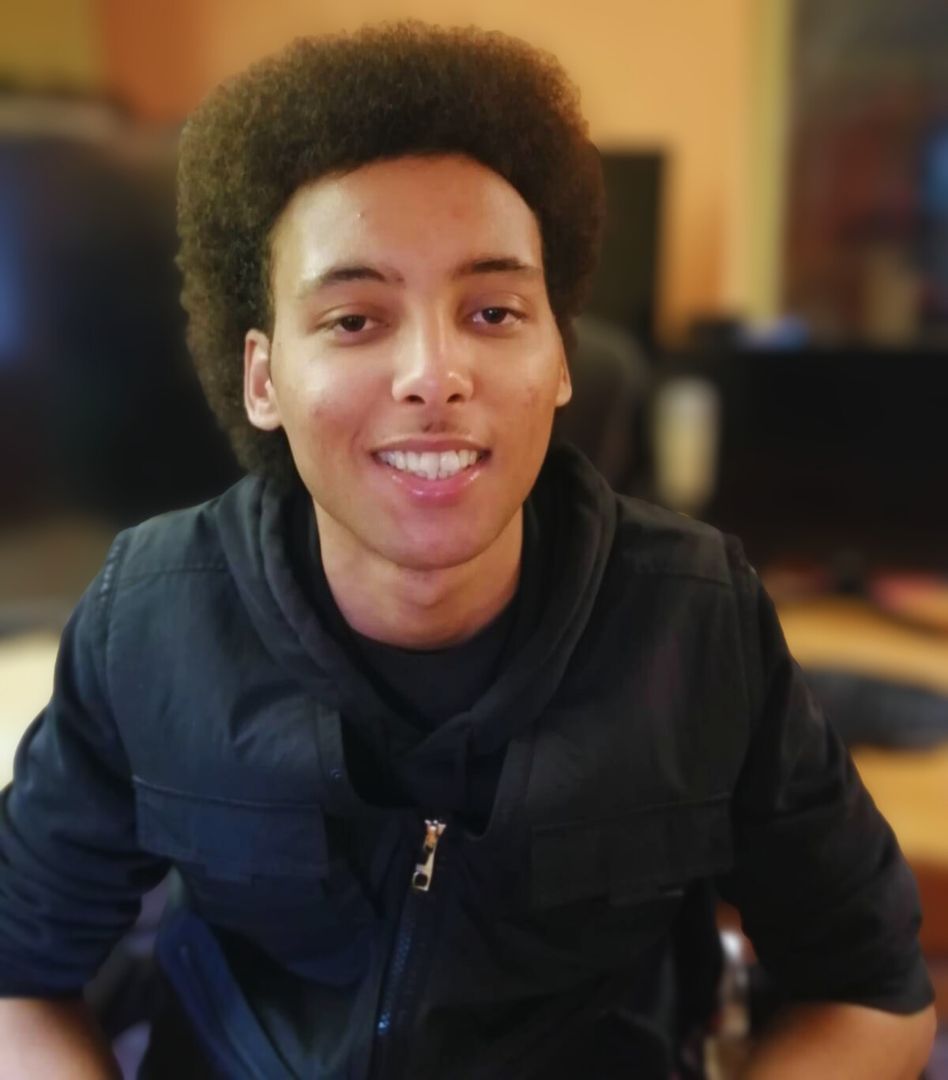 Photo of Manny Patterson, the Production Assistant and Creative Thinker at Beyond Face, smiling and looking directly at the camera with an out of focus background of an office