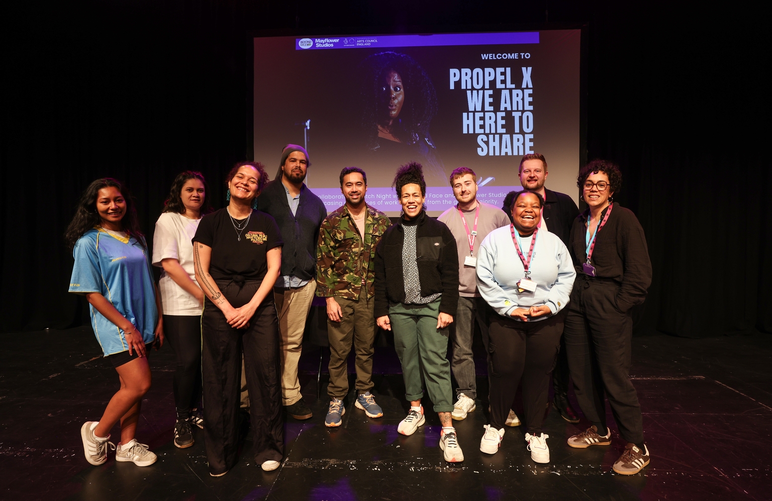 A group of artists stand in a semi circle smiling towards the camera 