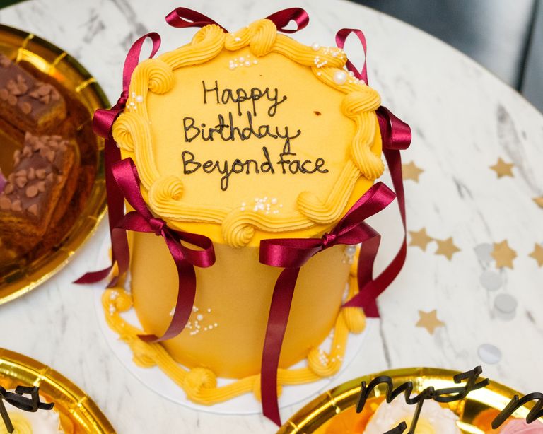 A yellow cake with red ribbons that reads Happy Birthday Beyond Face