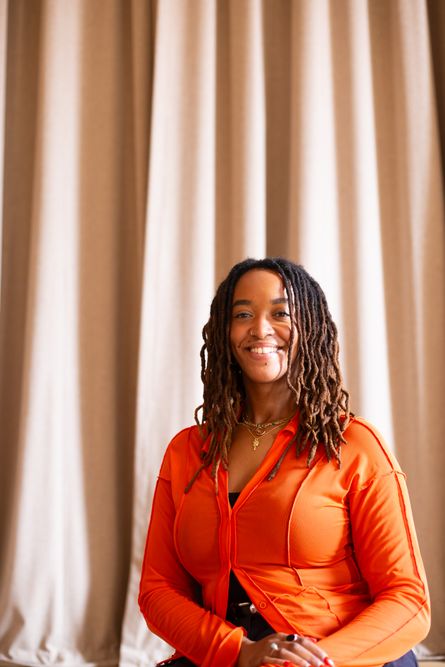 Photo of Tamera Heron, the Company Storyteller at Beyond Face, sitting in front of a curtain and smiling whilst looking directly at the camera