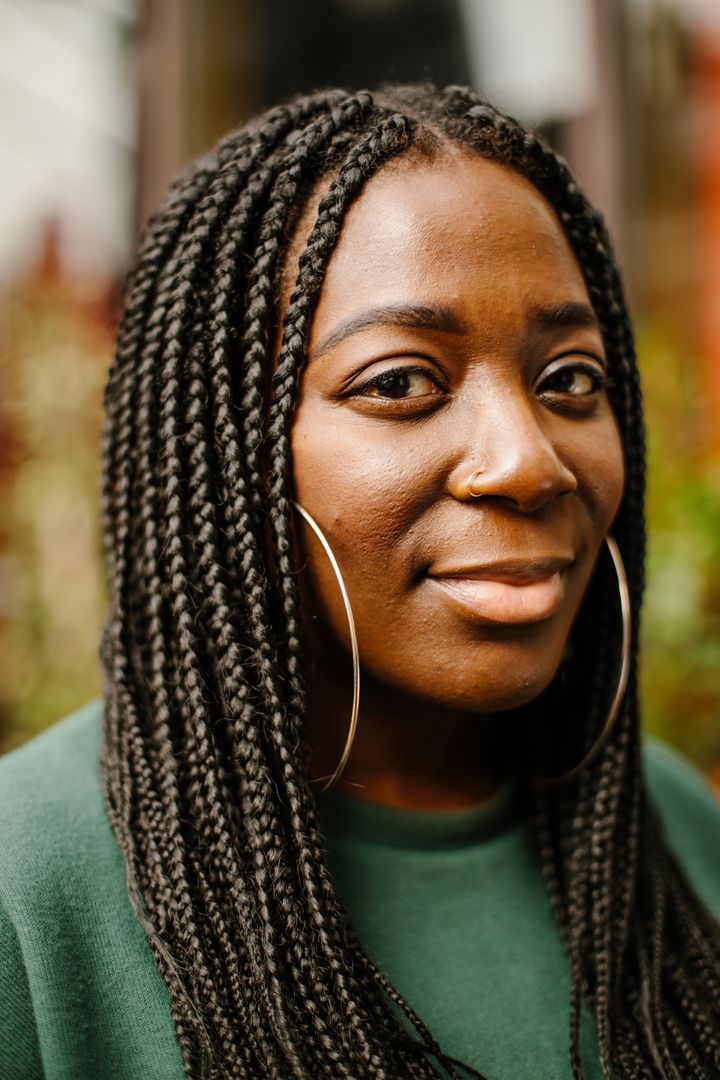 A woman with braids and large hold hoops smiles softly at the camera