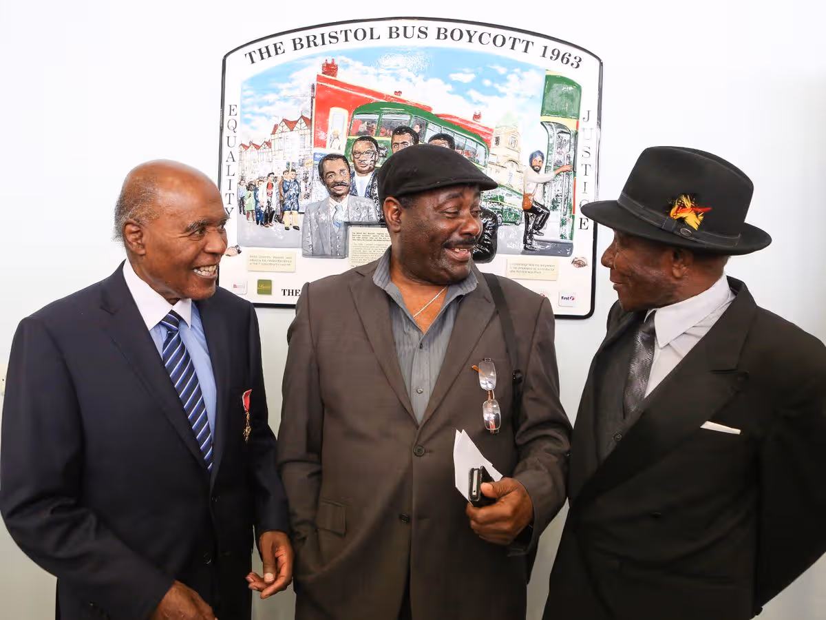 Three older black men stand in front of a plaque that reads 'The Bristol Bus Boycott 1963'