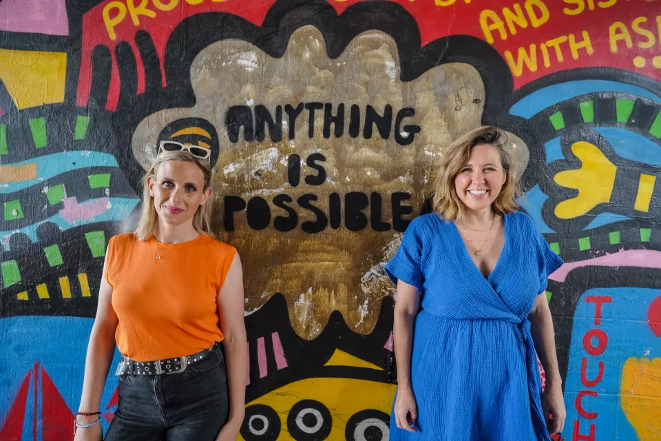 Two women stand near a wall with artwork that says 'Anything is Impossible'
