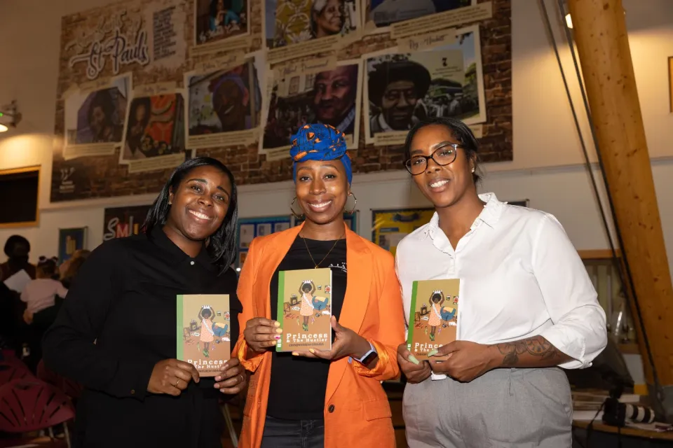 3 Black women pose holding the same book smiling at the camera
