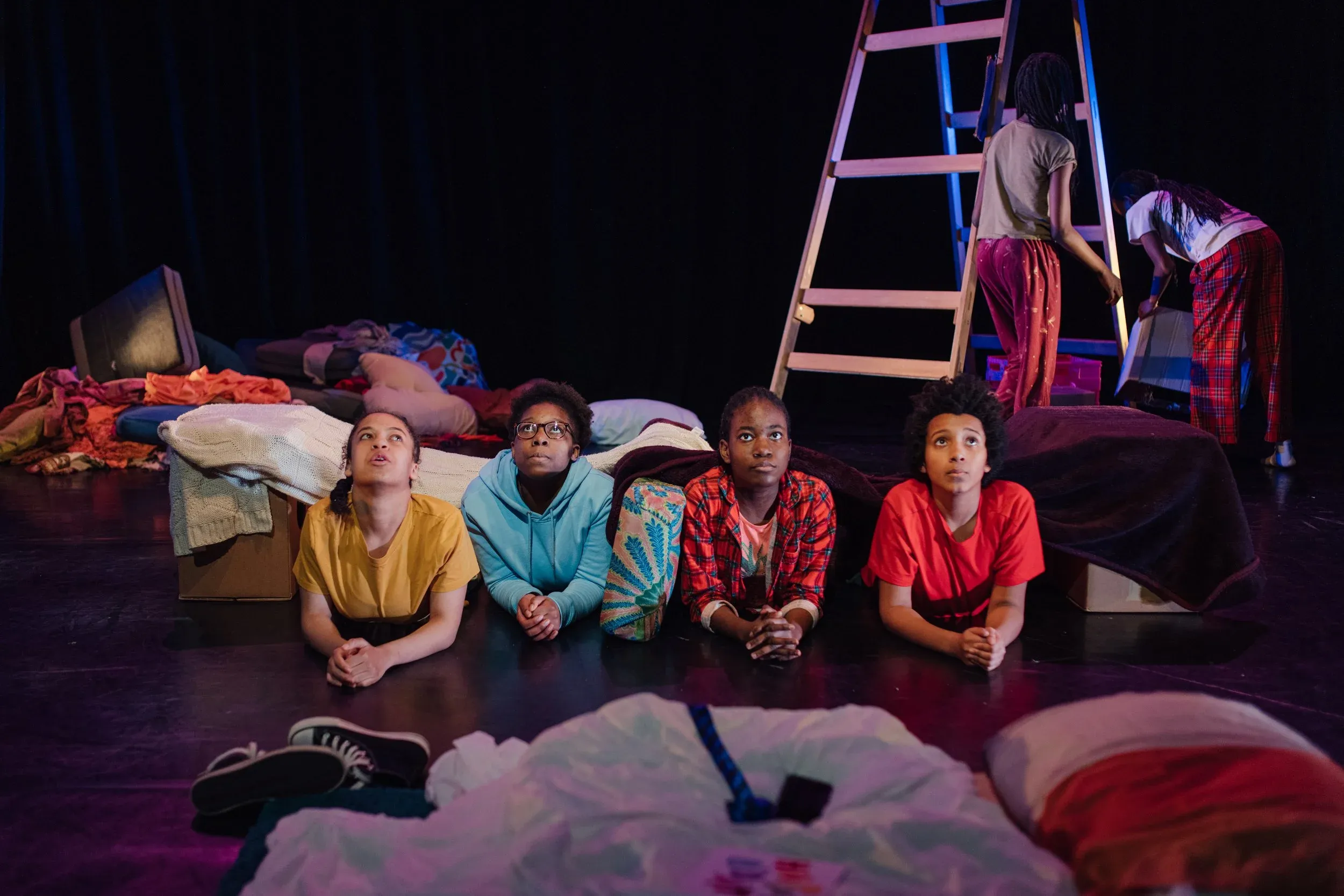 A group of young actors on stage and lying on the floor looking up at the sky