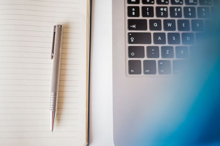 A notepad a pen placed next to the keys of a laptop