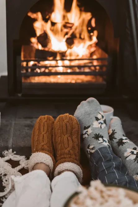 two feet in fluffy socks are warming by a fire