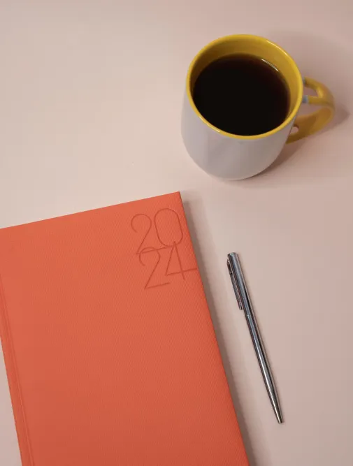 A 2024 diary placed on a table next to a coffee and a pen